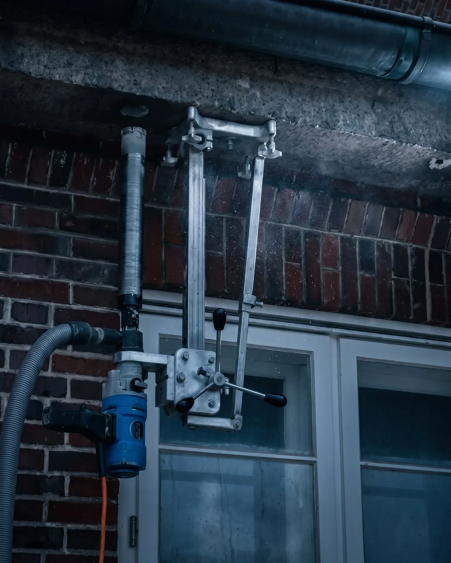 Kernbohrgerät mit Bohrständer an der Backsteinfassade eines Wohnhauses, über dem Fenster